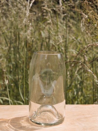 a clear vase on a table in front of summer grasses