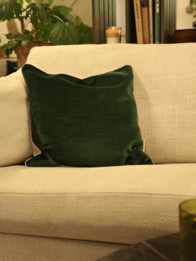 A natural green velvet cushion sitting on a cream woven sofa