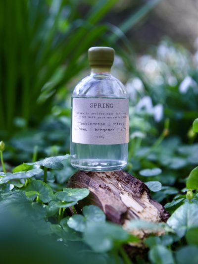 Spring reed diffuser refill bottle sitting on a log with spring greenery all around