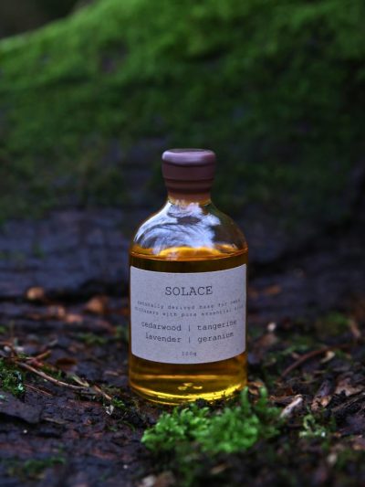 A lavender reed diffuser refill bottle sitting on a log